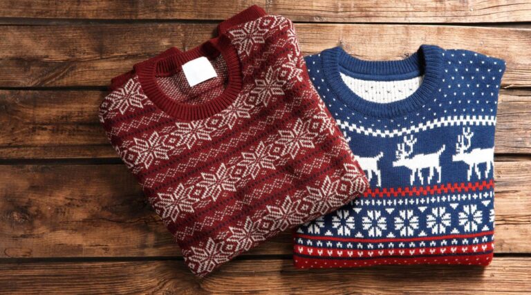 2 christmas jumpers folded and overlapping eachother are sat on a wooden surface. One is red and one is blue based, both with a scandi Christmassy feel